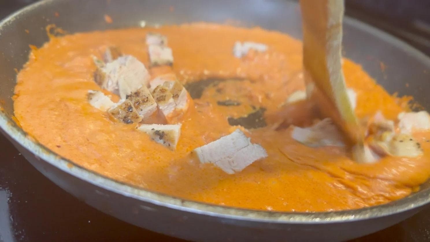 Creamy tomato sauce with diced chicken and grated Parmesan cheese being stirred in a pan
