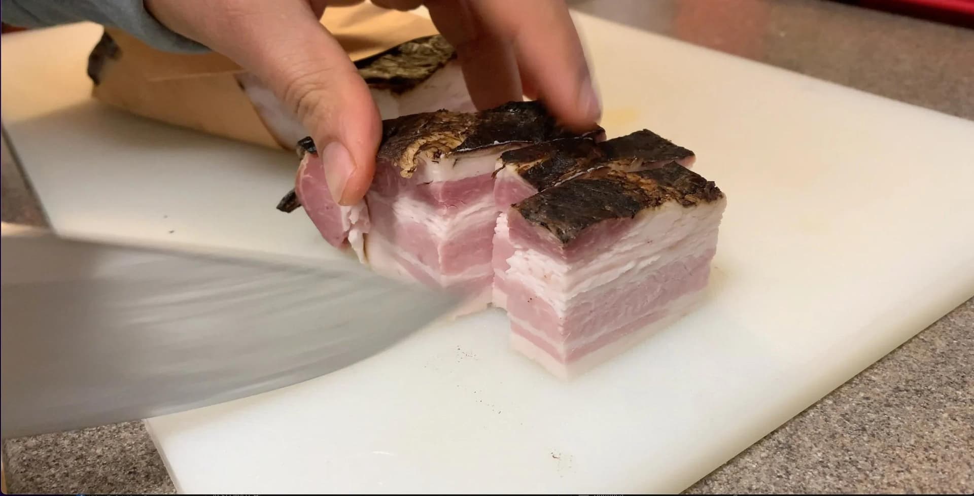 Hands cutting bacon lardons into cubes on a white cutting board for coq au vin.
