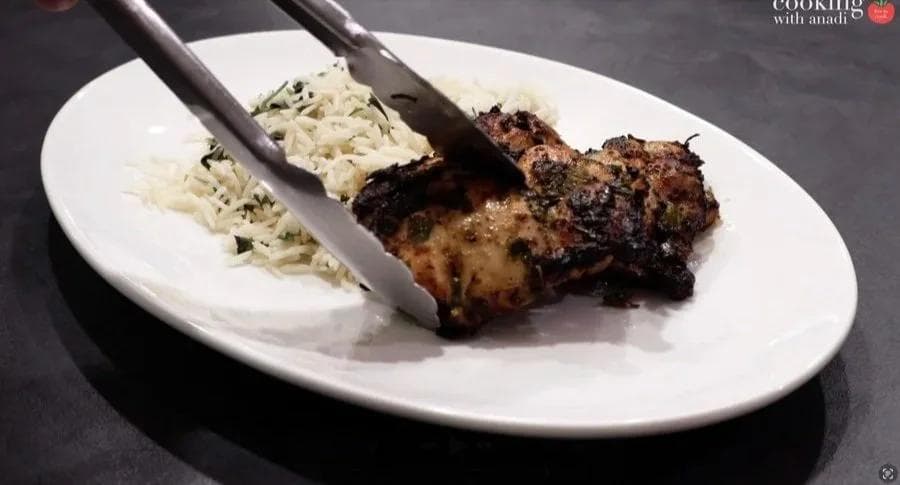 Plated Cuban mojo chicken with charred exterior served alongside white rice with herbs, tongs lifting a piece of chicken.