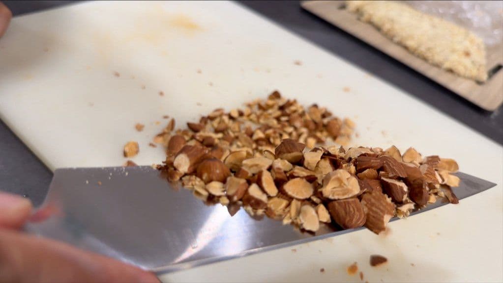Chopped roasted almonds on a white plate with a knife, prepared for salad assembly.