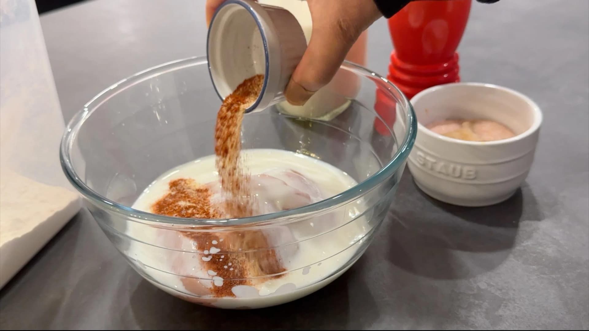 Spice mix being poured into a bowl of buttermilk and chicken tenders for marinating.