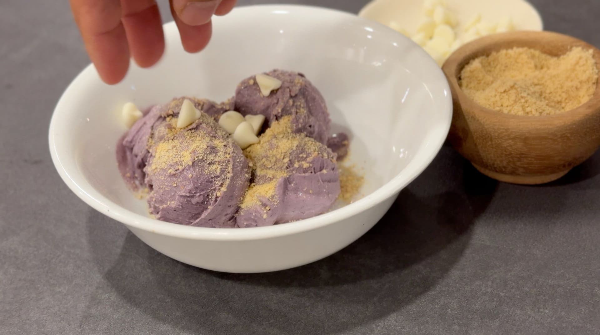 Purple blueberry protein ice cream scoops in a bowl topped with graham cracker crumbs and cream cheese chips.