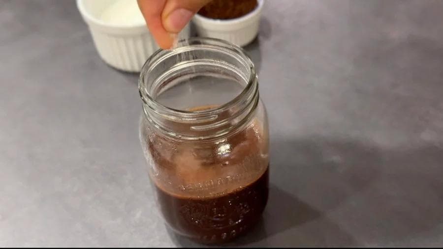 Homemade chocolate syrup in a mason jar with a hand holding the lid, ready to close.