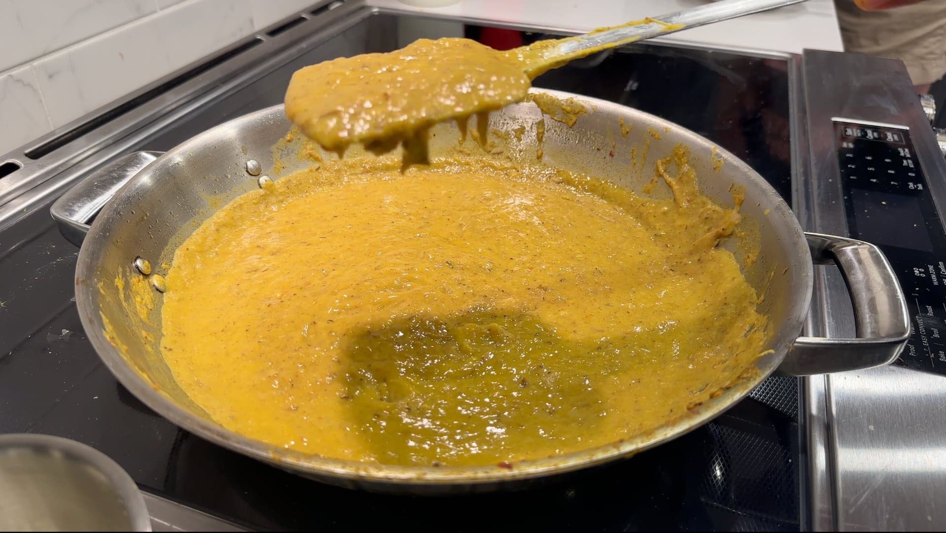Golden haleem mixture being stirred in a wok with ghee pooling in the center, showing the thick, mashed consistency of the dish.