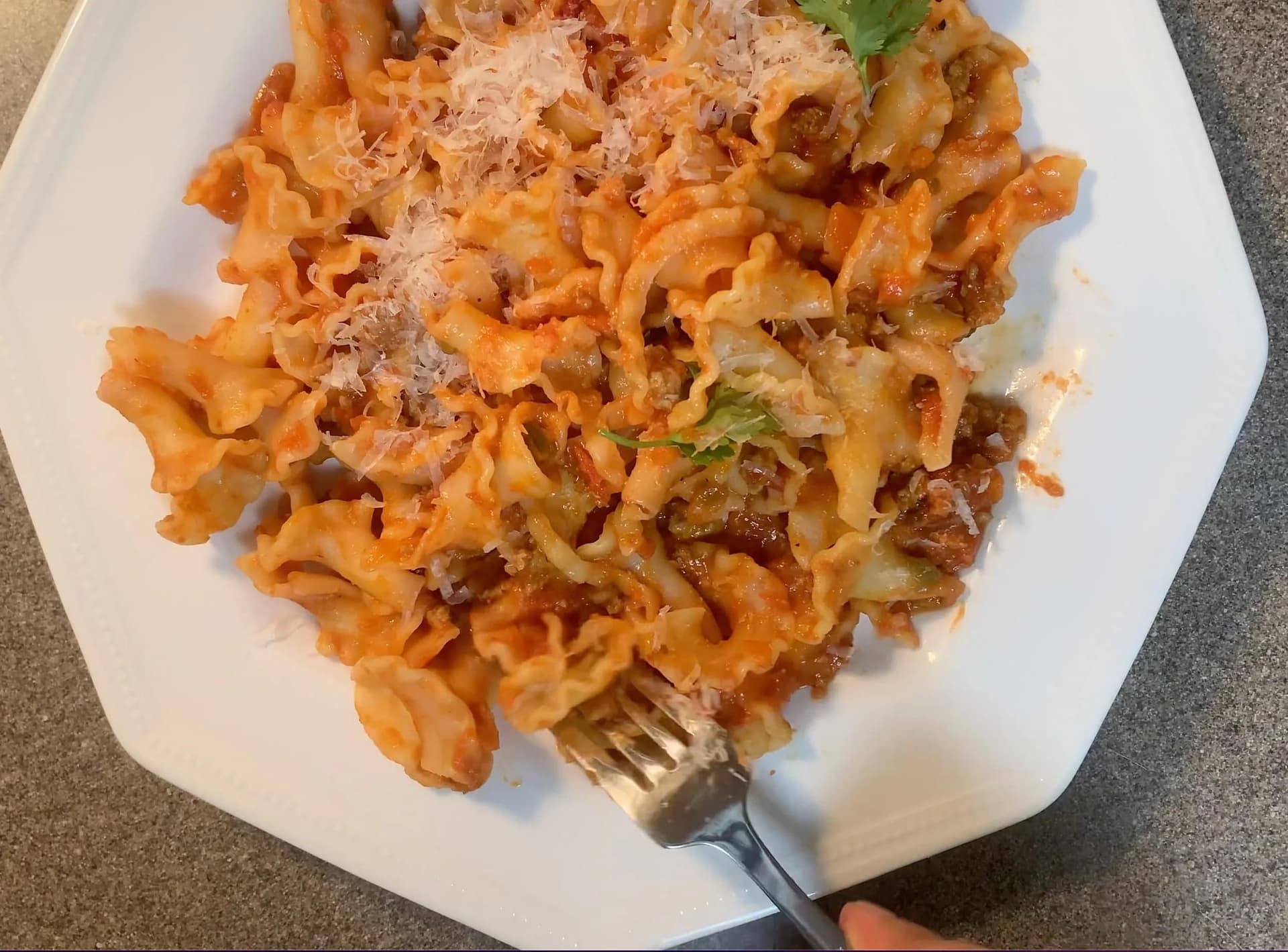 Indian-style chicken bolognese pasta topped with grated parmesan and cilantro on a white plate.