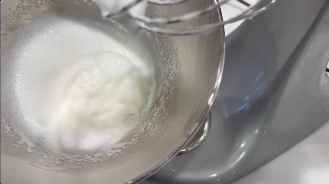 Fluffy egg white peaks being whisked in a stand mixer bowl for soufflé preparation.