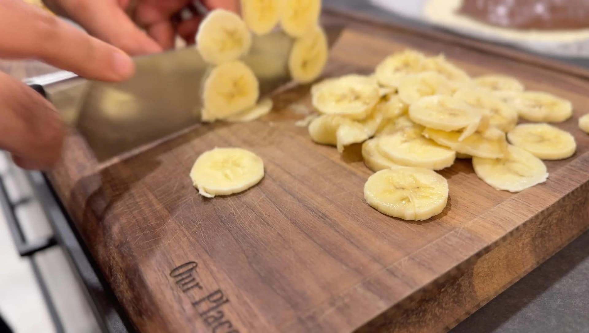 Thinly sliced banana rounds arranged over hazelnut spread on a wooden cutting board during galette preparation.