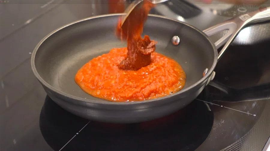 Red gochujang glaze simmering in a pan with a spatula stirring the mixture.