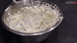 Whipped butter and cream cheese being mixed with a whisk in a metal bowl for sugar cookie glaze.
