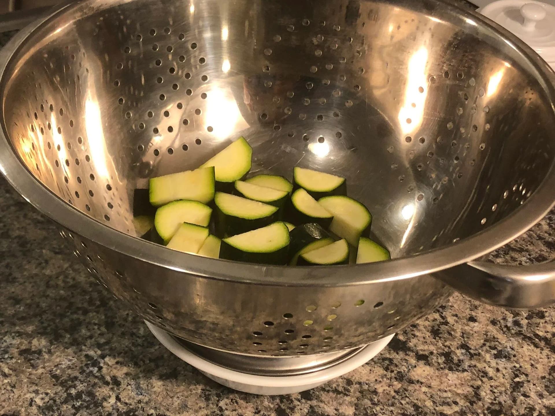 Diced zucchini slices in a metal colander ready for salting to remove excess moisture.