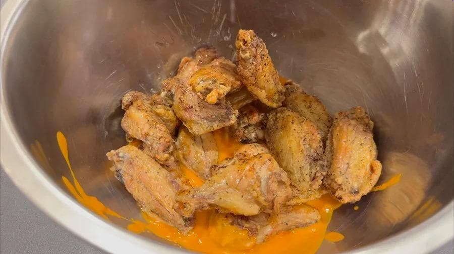Buffalo chicken wings coated in orange sauce in a stainless steel bowl, ready to serve.