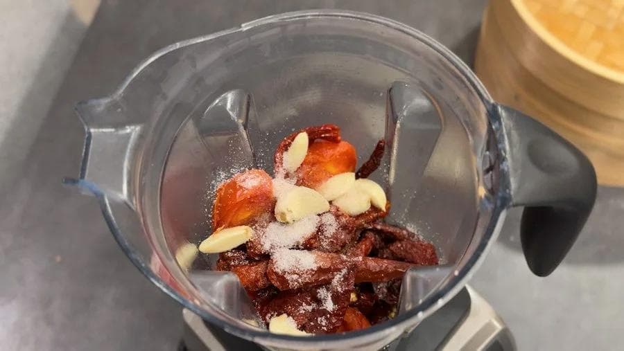 Ingredients for spicy momos chutney blended in a food processor, showing tomatoes, red chilies, cashews, and spices.
