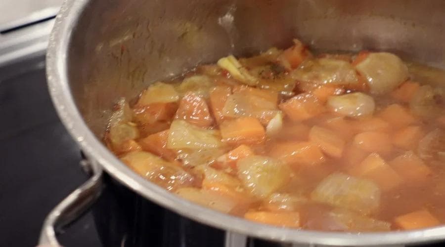 Diced carrots and potatoes simmering in broth in a pot during cooking.