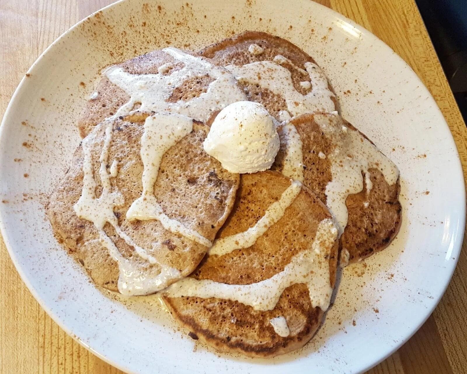 Stack of cinnamon pancakes topped with butter and powdered sugar on a white speckled plate.