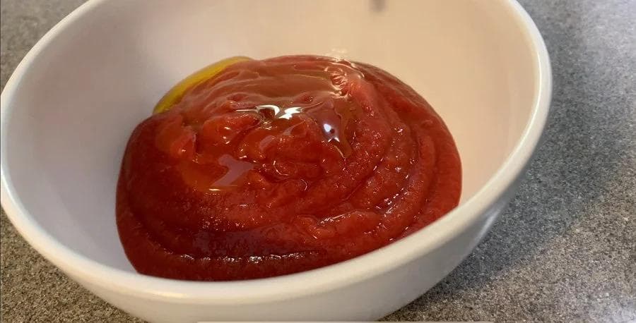 Red pizza sauce mixed in a white bowl with a drizzle of golden oil on top.