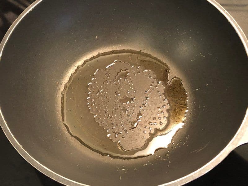 Cumin seeds and hing sizzling in hot oil in a pan, releasing aromatics for the potato wrap filling.