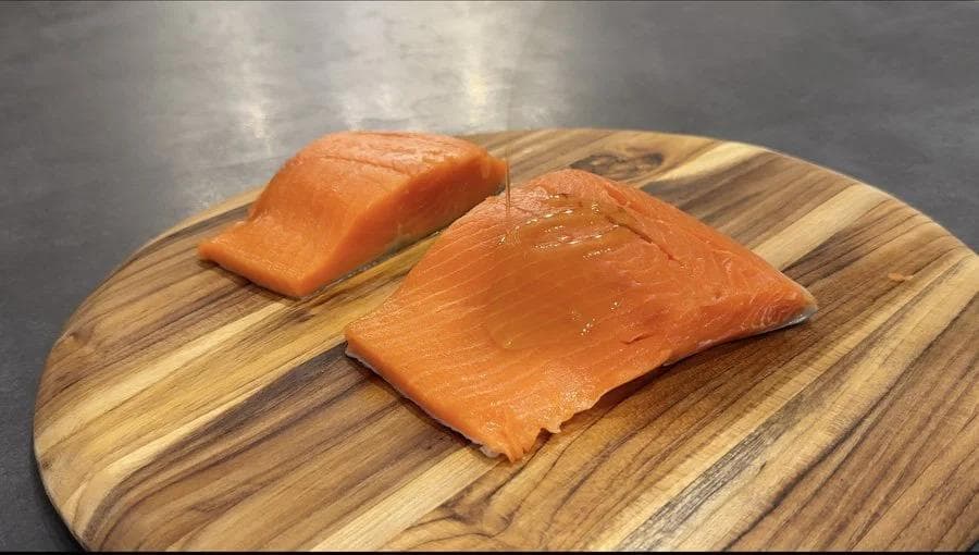Two salmon fillets on a wooden cutting board, seasoned and ready for air frying.
