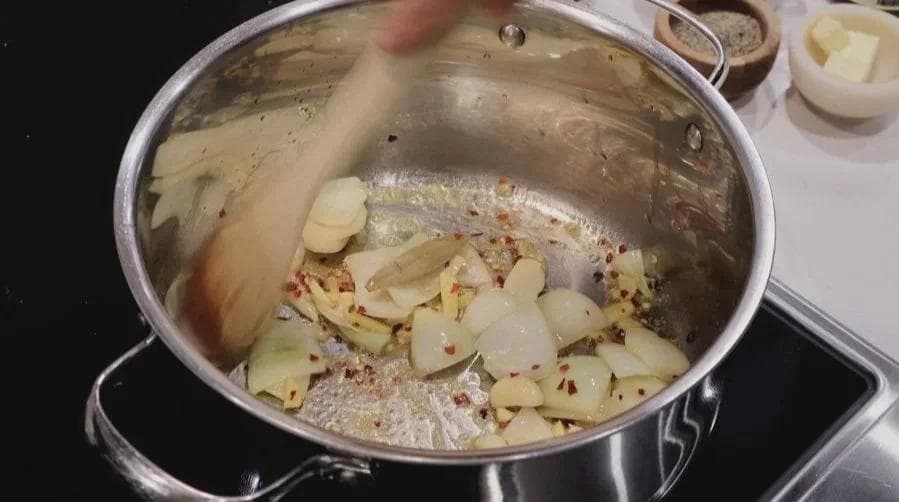 Diced onions and carrots cooking in a pot with red chili flakes and salt on the stovetop.