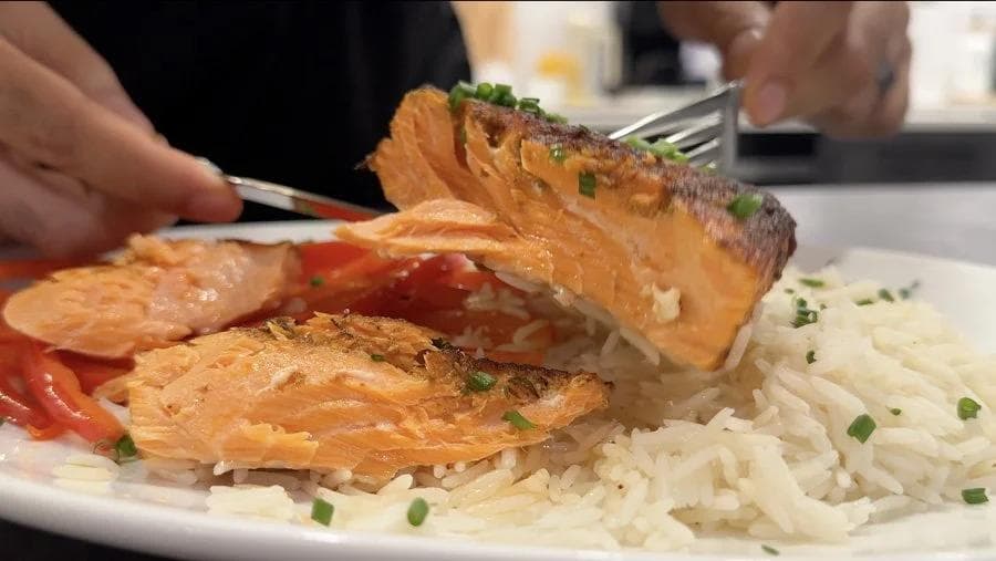 Air fryer salmon fillet being lifted on a fork, served over rice with red peppers and garnished with green onions.