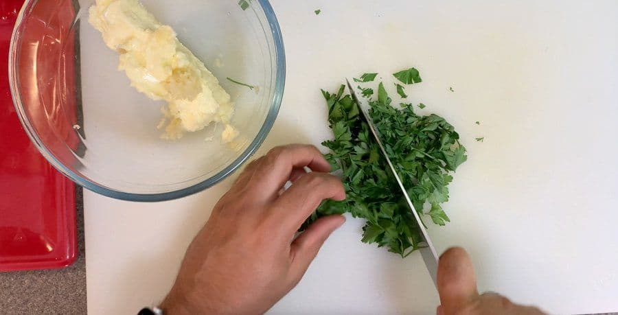 Hands chopping fresh parsley next to a bowl of mixed garlic butter ingredients for air fryer fries.