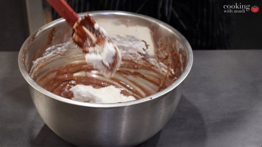 Folding whipped egg whites into chocolate mixture with a red spatula in a metal bowl.