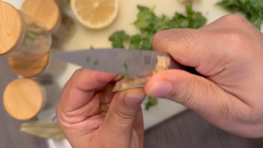 Hands holding a knife, mincing fresh cilantro on a cutting board with lemon slices and herbs nearby.