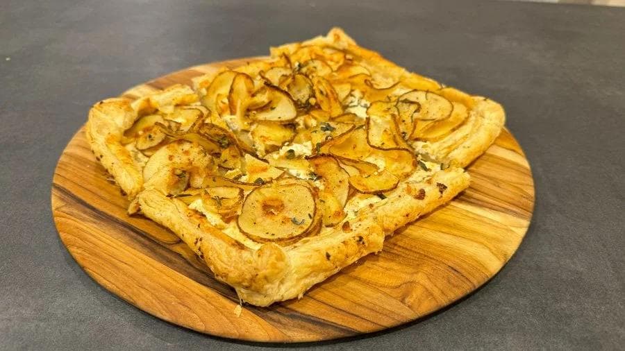 Baked puff pastry tart with sliced potatoes and ricotta on a wooden board.