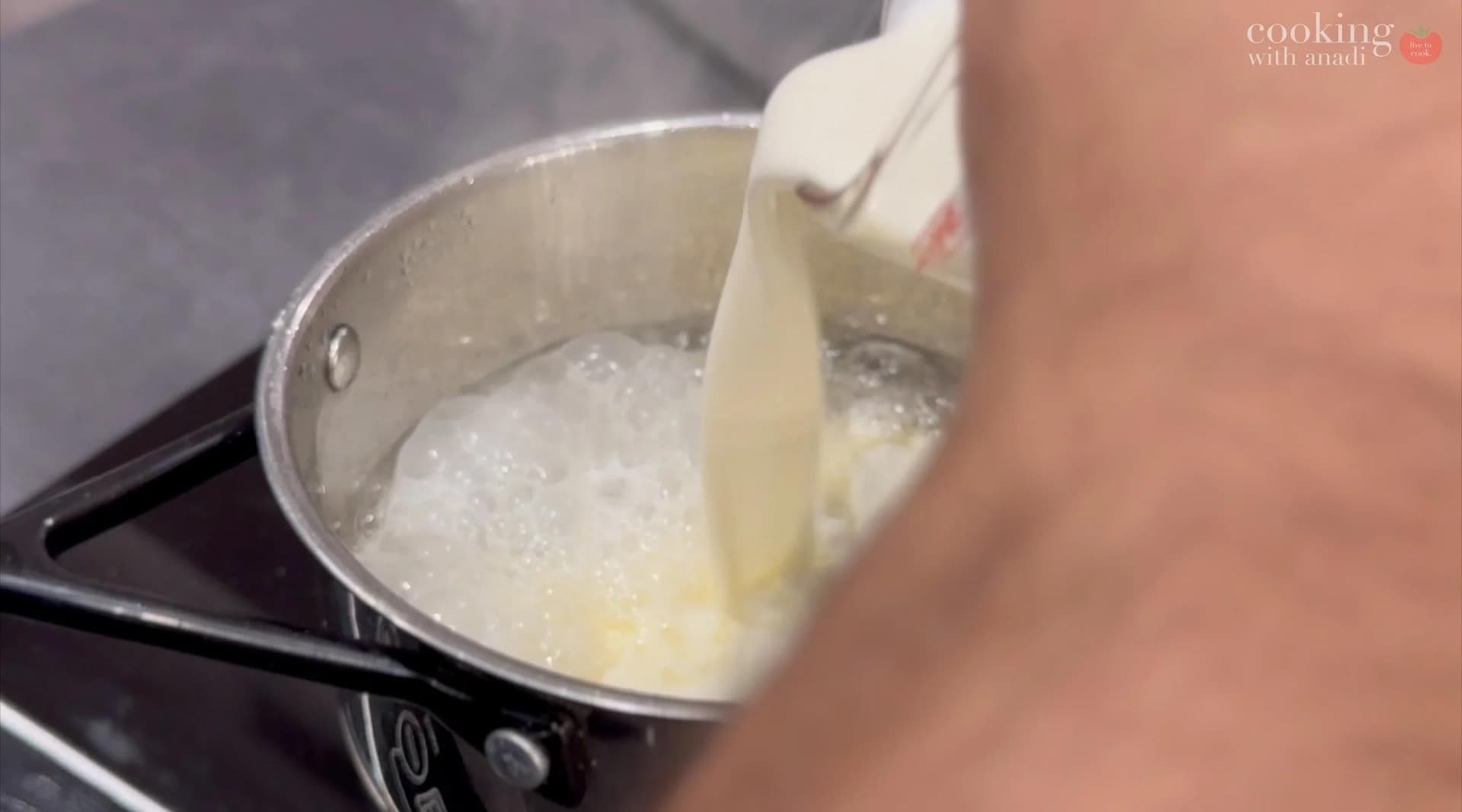 Pouring cream into caramel sauce while whisking in a saucepan on stovetop.