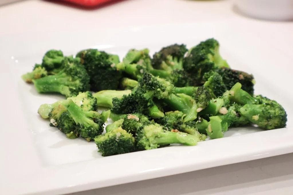 Garlic butter broccoli florets on a white plate, coated with seasoning and melted butter.