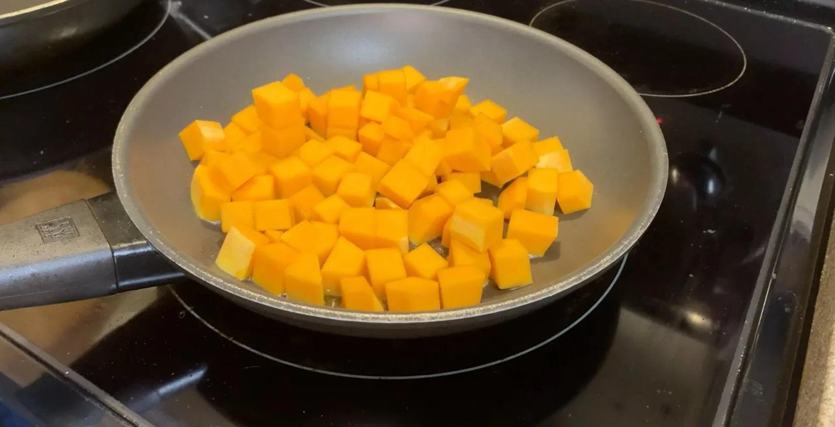 Diced yellow squash in a pan being sautéed in olive oil on a stovetop.
