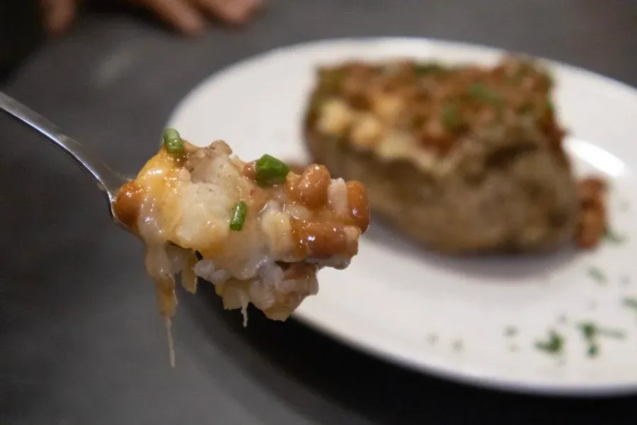 Spoonful of loaded jacket potato with melted cheese, beans, and green onions, with plated potato in background