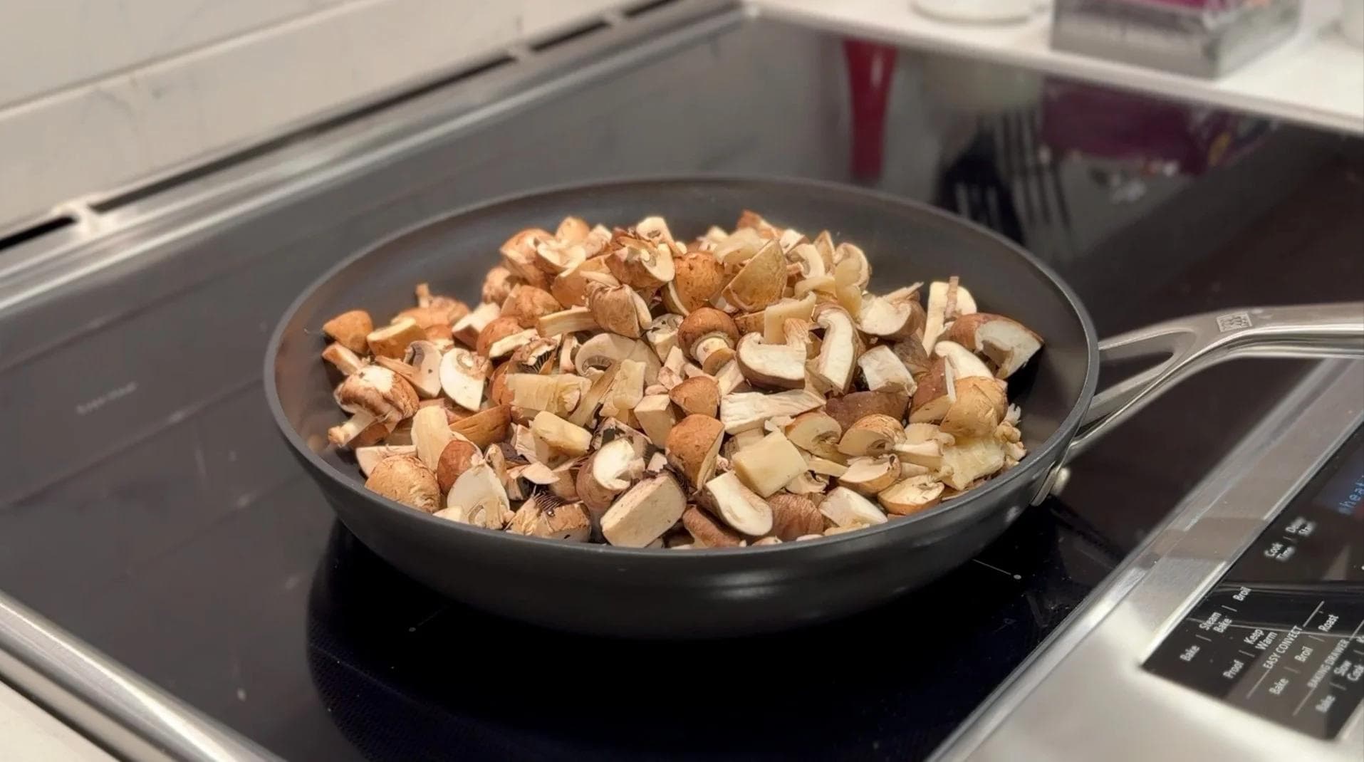 Diced mushrooms cooking in a black skillet on a stovetop induction cooker.