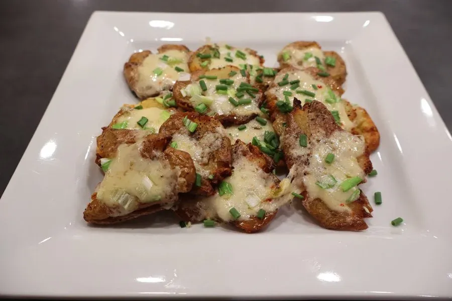 Crispy air fryer smashed potatoes topped with melted cheese and green onions on a white plate