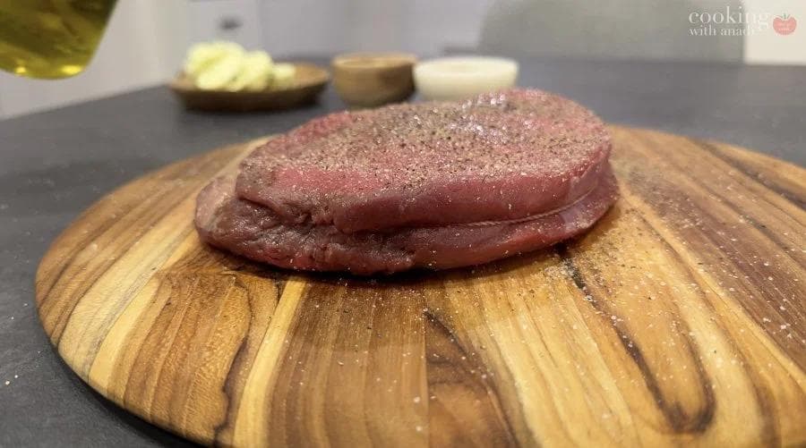 Raw sirloin steak seasoned with salt and pepper on a wooden cutting board, ready for air frying.