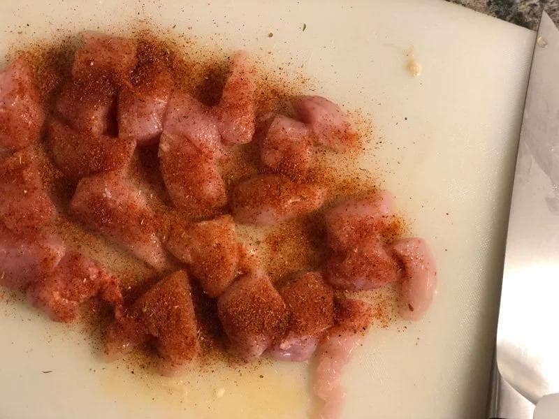 Cubed chicken breast seasoned with Cajun spice blend on a white cutting board.