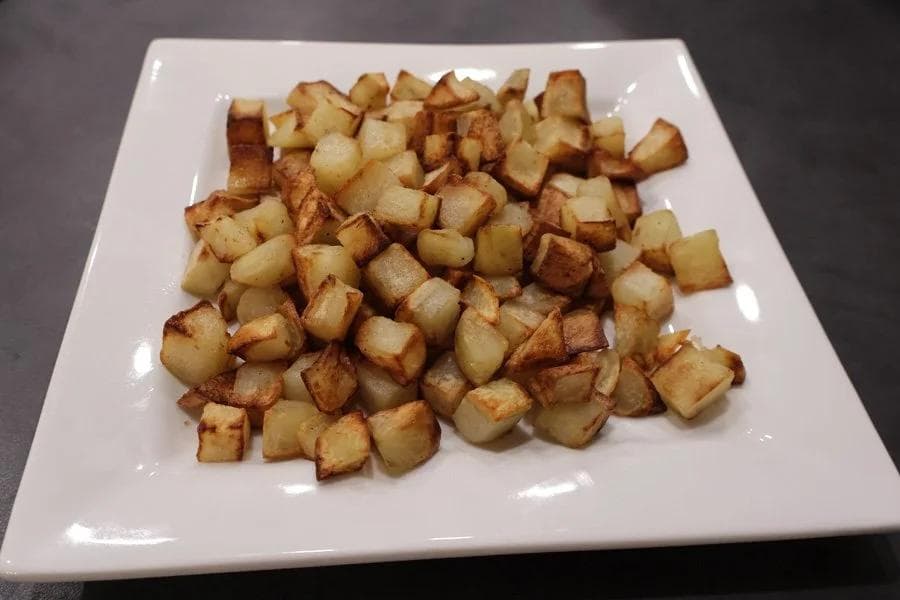 Crispy golden air fryer roasted potato cubes served on a white square plate.
