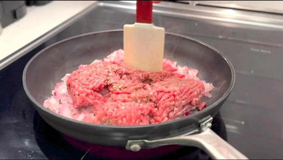 Ground beef cooking in a skillet with a spatula breaking it into pieces, browning on medium heat.