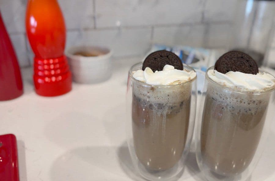Two tall glasses of Cookies and Cream Oreo latte with whipped cream and Oreo cookies on top.