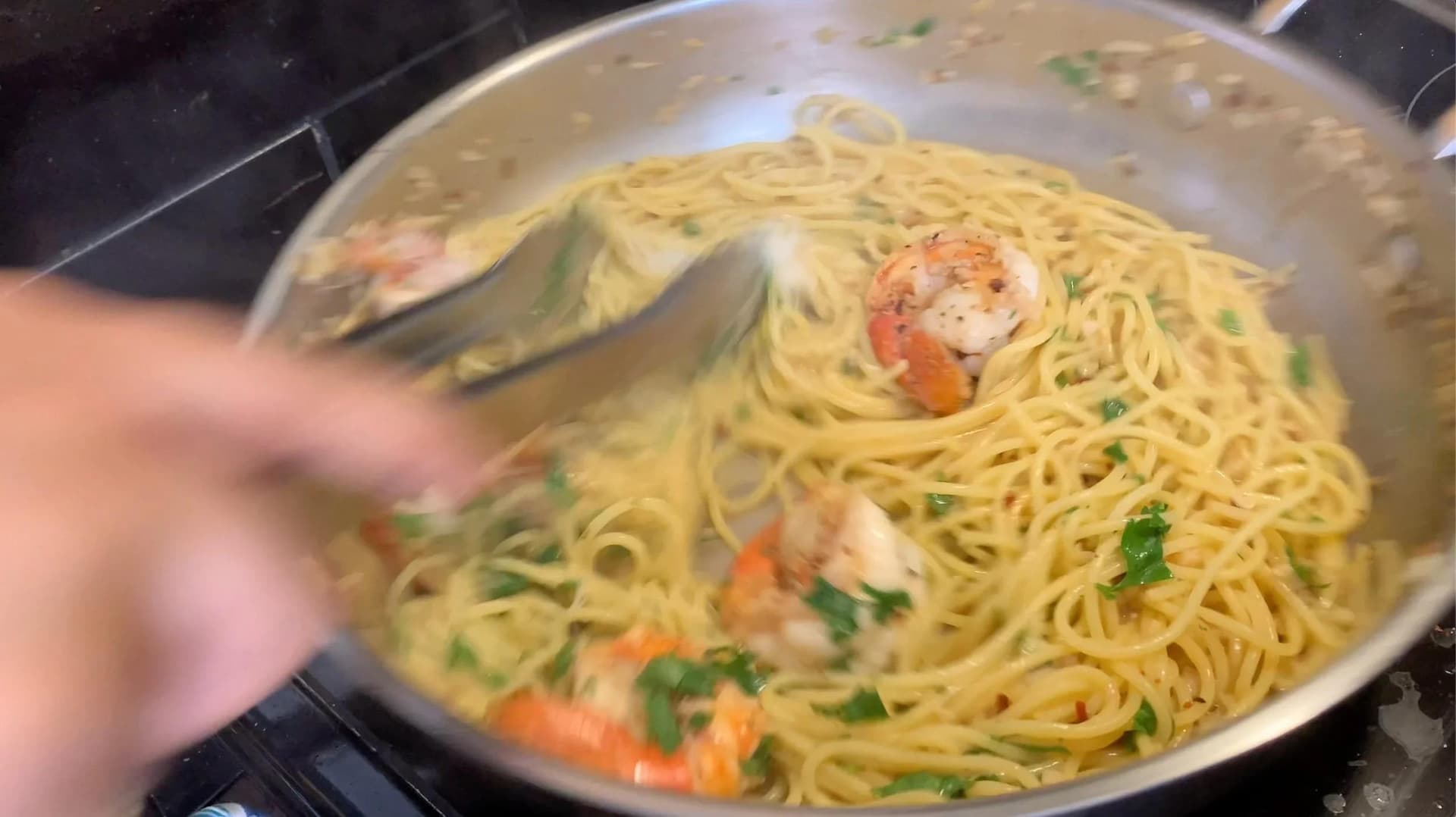 White wine lemon garlic shrimp scampi with pasta being mixed with parsley and parmesan cheese in a pan.