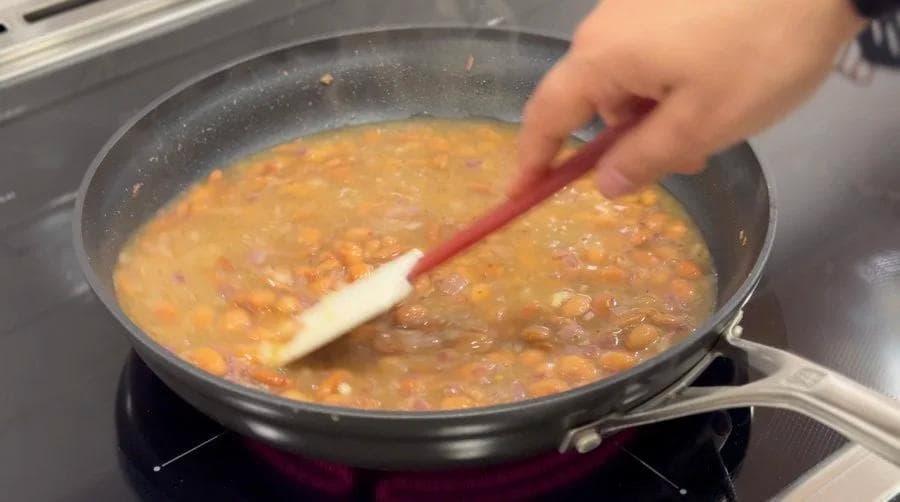 Stirring simmering refried beans in a skillet with a spatula during the cooking process.