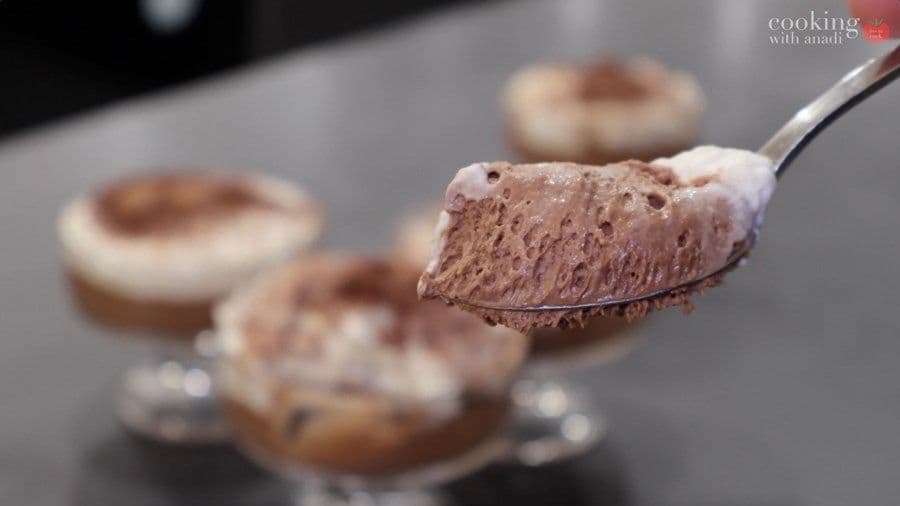 Chocolate mousse being spooned onto a dessert plate, showing creamy texture with whipped cream topping and cocoa powder dusting.