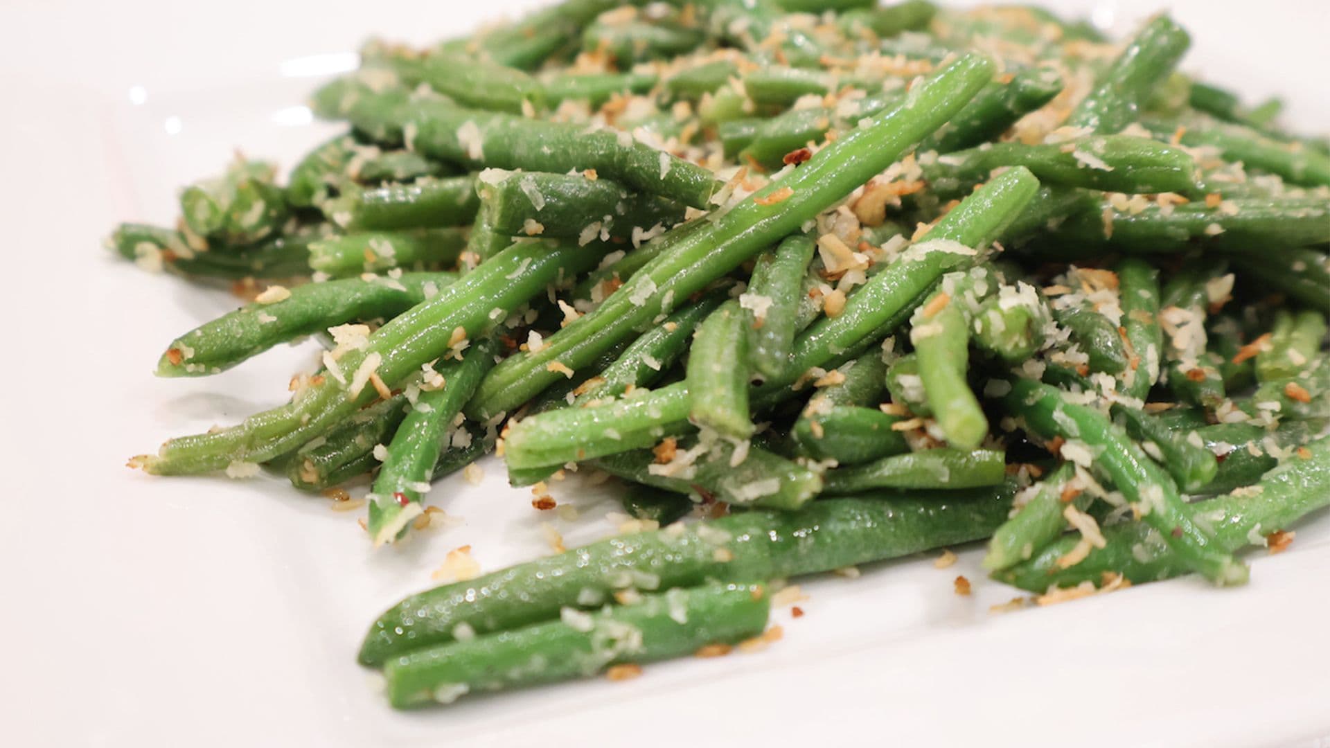 Sautéed green beans topped with toasted coconut flakes and garlic on a white plate.