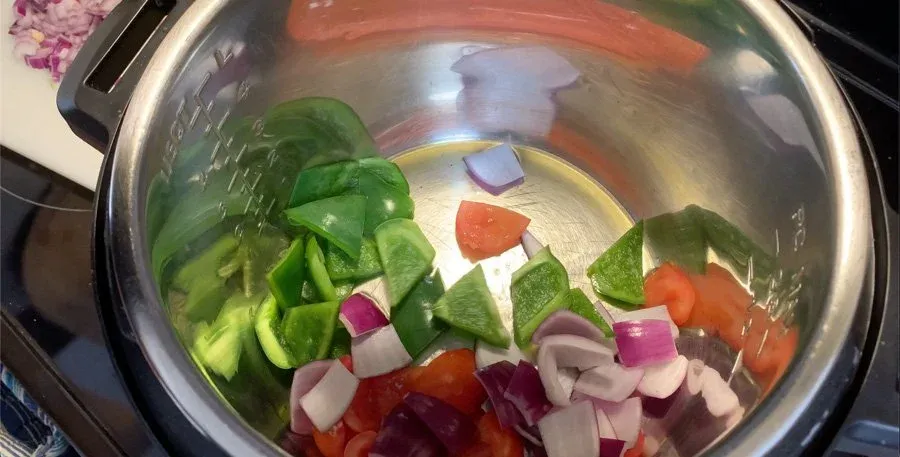 Raw vegetables in Instant Pot: sliced cucumbers, bell peppers, and diced red onions ready for sautéing.