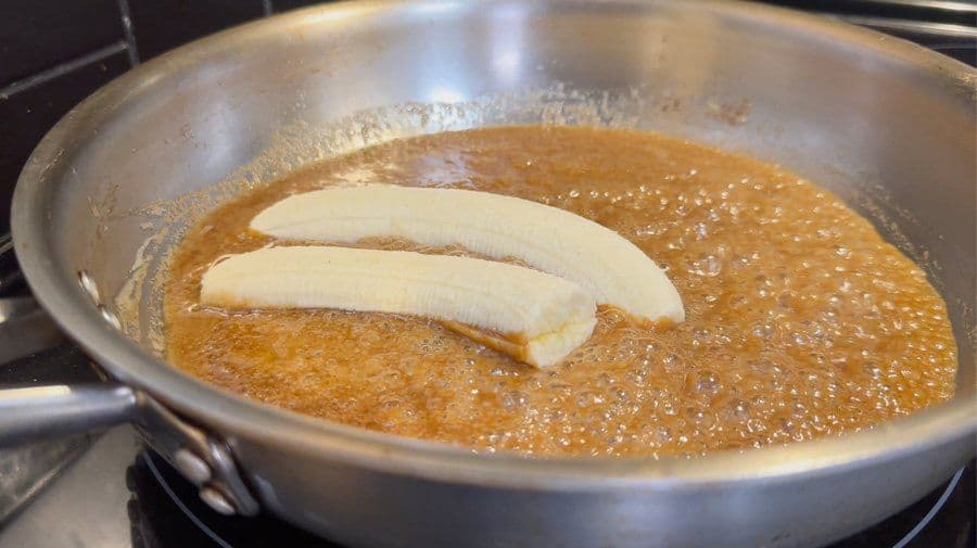 Banana slices warming in apple pie spiced caramel sauce in a skillet on the stovetop.