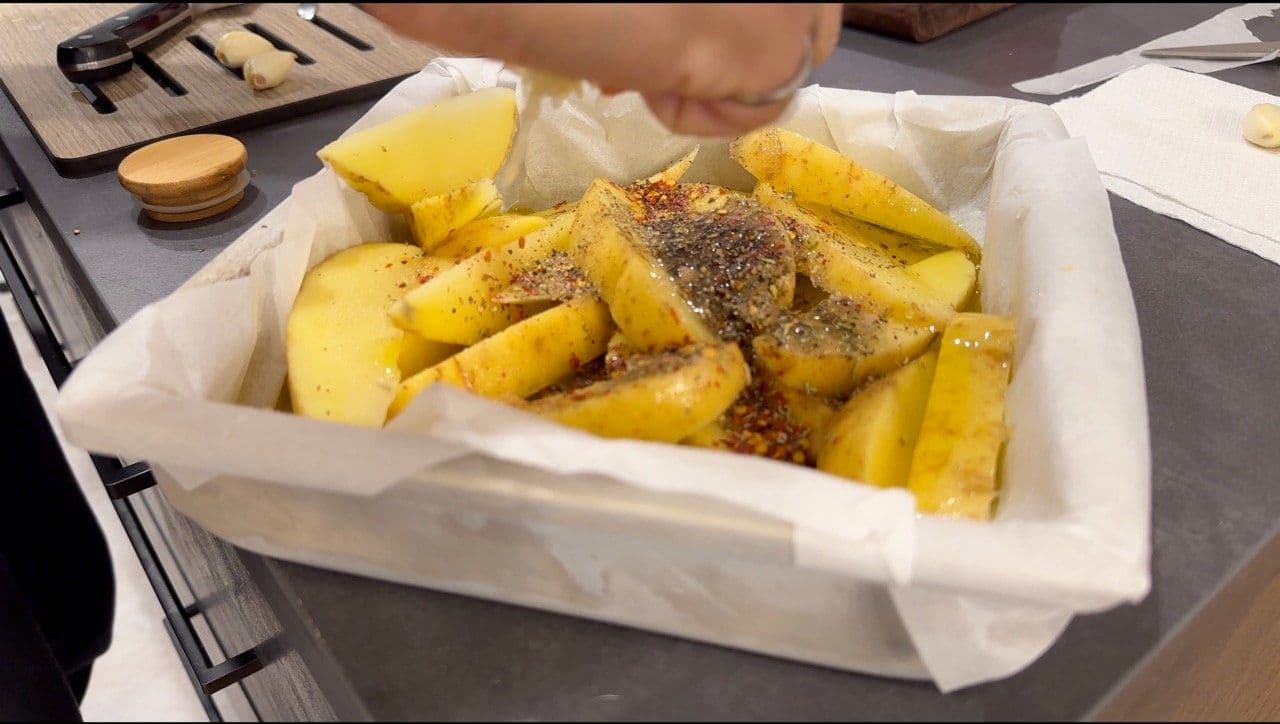 Baked Greek lemon potatoes in a white container, golden and seasoned with herbs and spices.