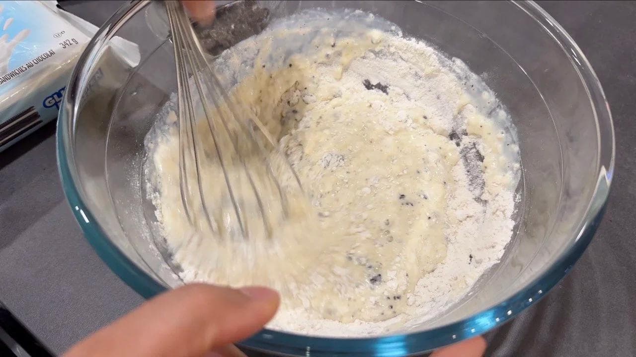 Whisking crushed Oreo cookies into thick gluten-free pancake batter in a glass bowl.