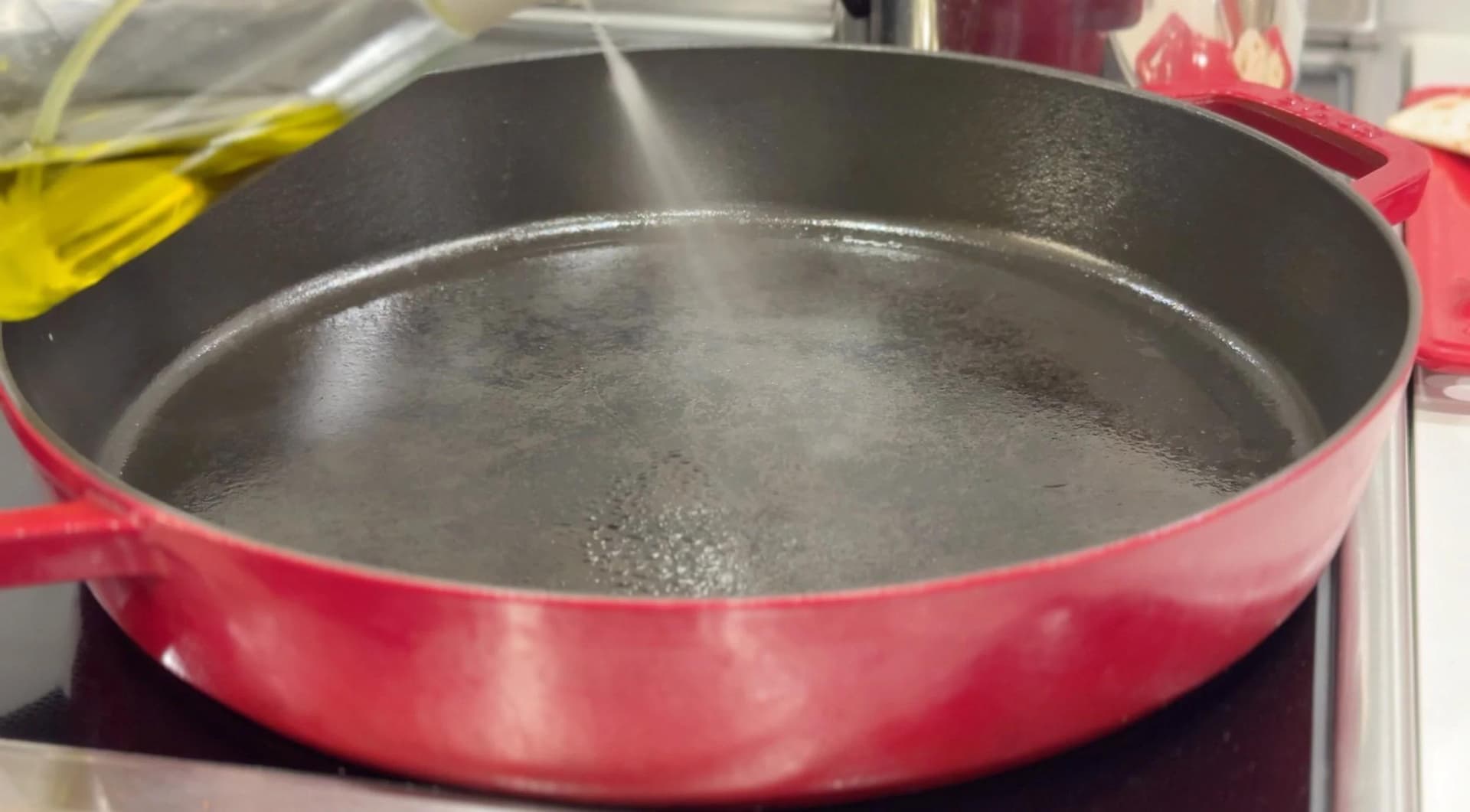 Pink cast iron skillet with water heating on stovetop, ready for cooking burger patties.