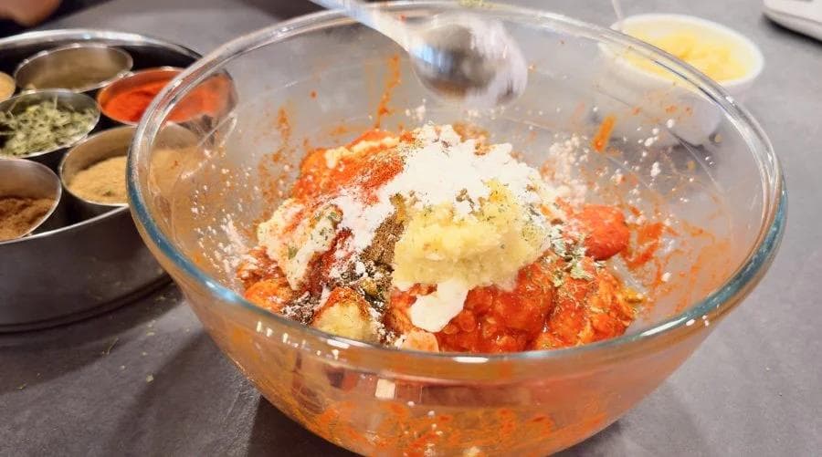 Glass bowl with tandoori marinade ingredients mixed together including yogurt, spices, and seasonings for chicken marinade.