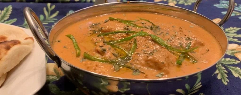 Chicken Changezi in a copper bowl with creamy tomato sauce, garnished with green chilis and cilantro.