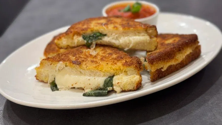 Three slices of golden-brown mozzarella in carrozza stacked on a white plate with a small bowl of red sauce.